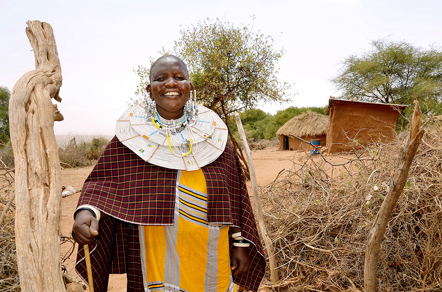 Mama Neema stands at the entrance of her traditional boma (homestead) where she built three houses for her family in Kimokouwa village in Arusha, Tanzania UN WOMEN